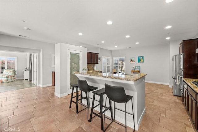 kitchen featuring a breakfast bar, decorative backsplash, kitchen peninsula, stainless steel appliances, and light stone countertops