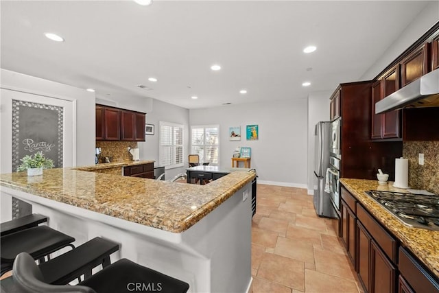 kitchen with a breakfast bar, appliances with stainless steel finishes, tasteful backsplash, light stone countertops, and exhaust hood