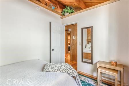 bedroom featuring hardwood / wood-style floors, vaulted ceiling with beams, and wooden ceiling