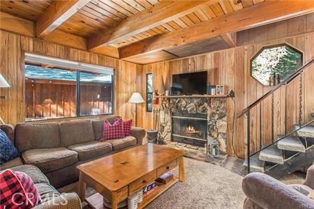 living room with carpet flooring, beam ceiling, wooden ceiling, a stone fireplace, and wood walls