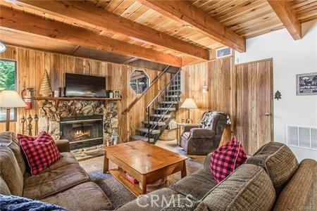 living room with beam ceiling, wooden walls, a fireplace, and wood ceiling