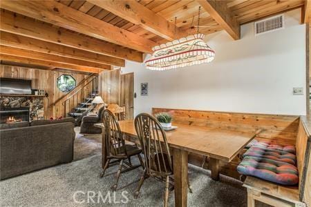 carpeted dining space with beamed ceiling, a fireplace, wood walls, and wood ceiling