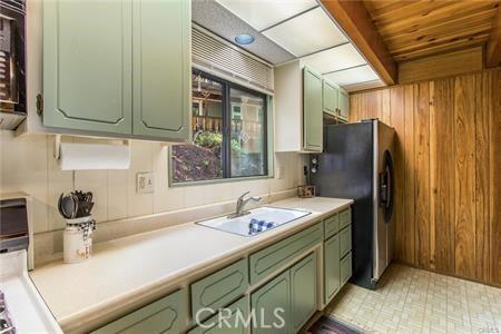 kitchen featuring stainless steel fridge, wood ceiling, sink, green cabinetry, and wood walls