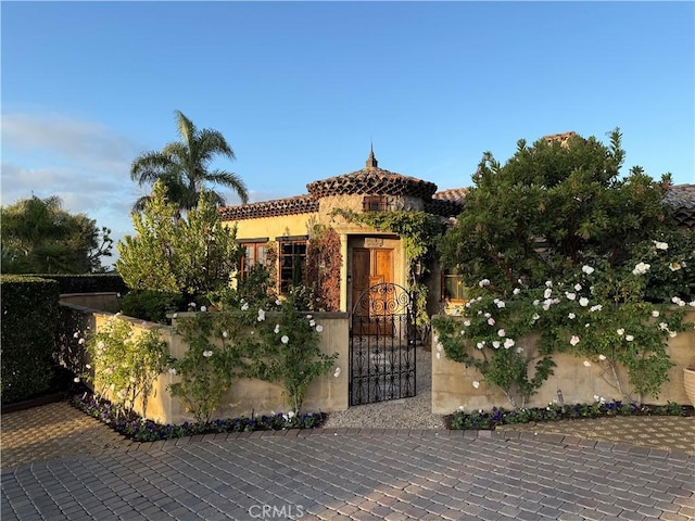 mediterranean / spanish-style home with a tiled roof, a fenced front yard, a gate, and stucco siding