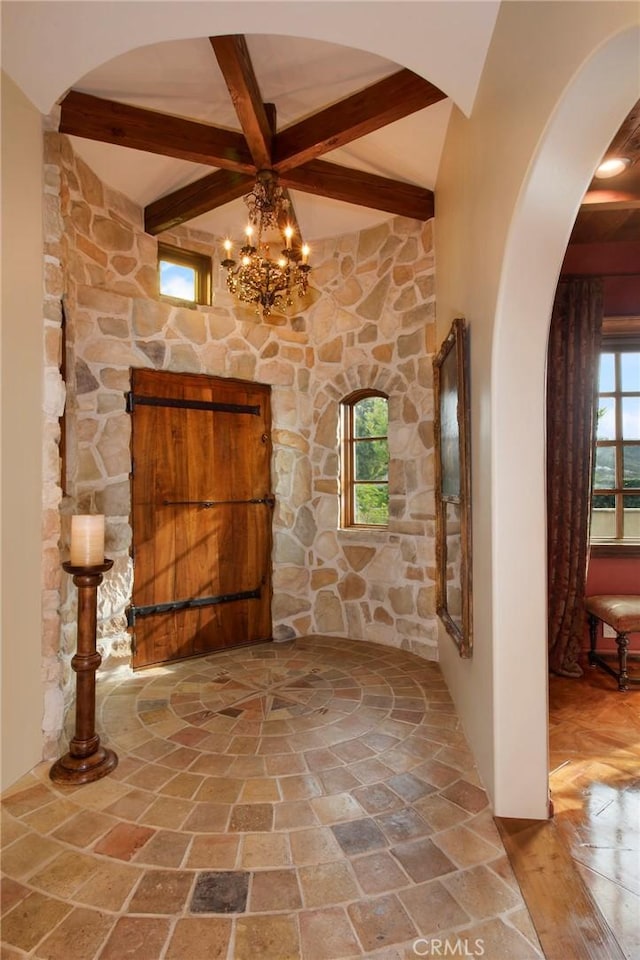 interior space with a chandelier, arched walkways, and beam ceiling
