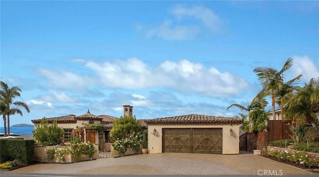 mediterranean / spanish-style house featuring a tile roof, decorative driveway, an attached garage, fence, and stucco siding
