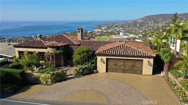 mediterranean / spanish-style home featuring a tiled roof, an attached garage, fence, decorative driveway, and stucco siding