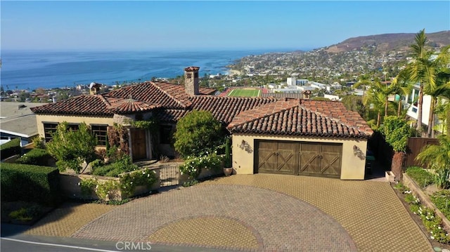 mediterranean / spanish house with a tile roof, a water view, a chimney, fence, and stucco siding