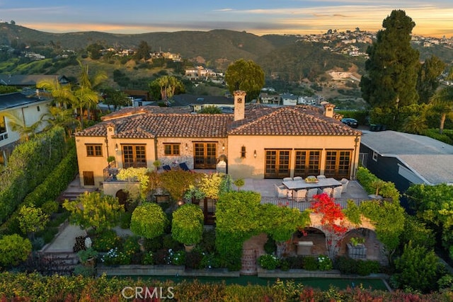 1330 Temple Hills Dr, Laguna Beach, CA 92651 - back of property at dusk featuring french doors, a chimney, a tiled roof, and stucco siding