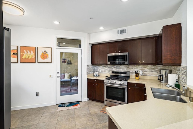 kitchen featuring dark brown cabinetry, sink, stainless steel appliances, tasteful backsplash, and light tile patterned flooring