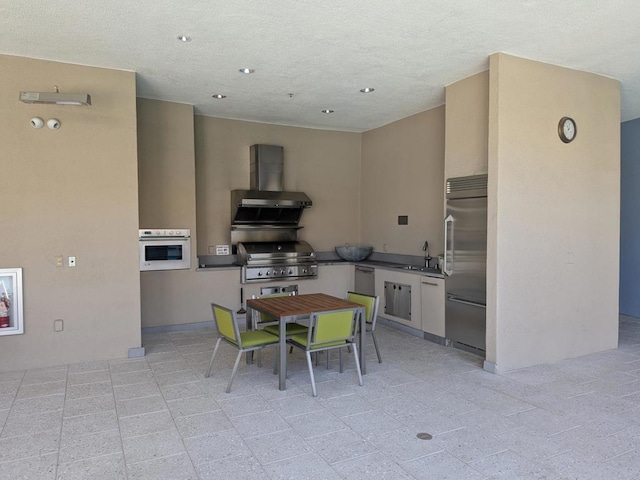 kitchen featuring white oven, built in fridge, sink, white cabinetry, and extractor fan