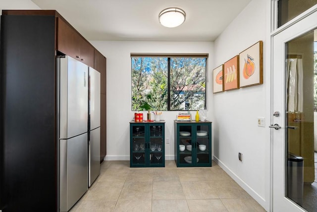 interior space featuring dark brown cabinets, stainless steel refrigerator, and light tile patterned flooring