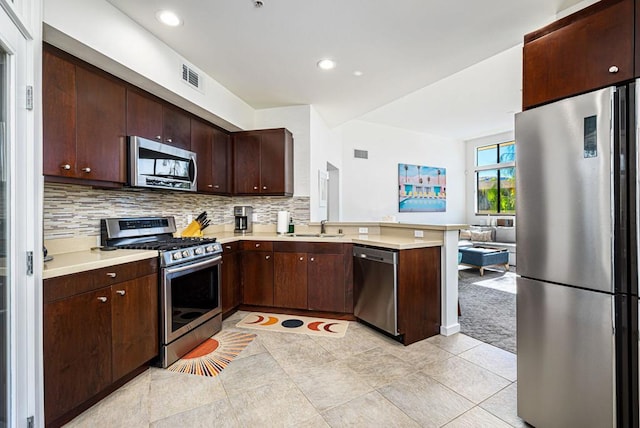 kitchen featuring kitchen peninsula, backsplash, dark brown cabinets, stainless steel appliances, and sink