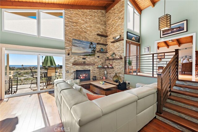 living room featuring beam ceiling, hardwood / wood-style floors, a stone fireplace, and wooden ceiling