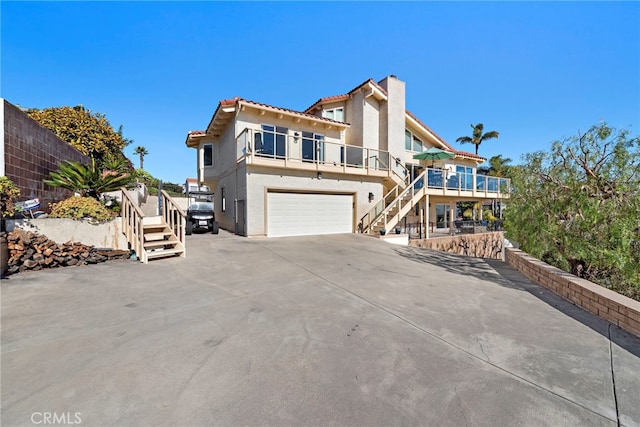 view of front of house featuring stucco siding, stairway, concrete driveway, an attached garage, and a chimney