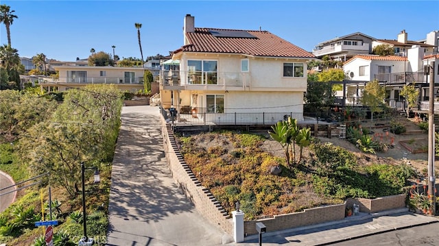 rear view of house featuring stucco siding, roof mounted solar panels, a balcony, a chimney, and a tiled roof