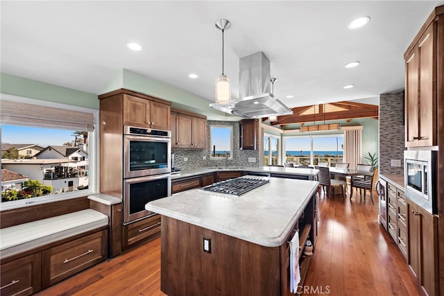 kitchen with island range hood, decorative light fixtures, appliances with stainless steel finishes, a kitchen island, and backsplash