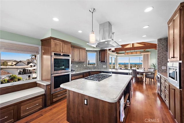 kitchen with island exhaust hood, a kitchen island, backsplash, appliances with stainless steel finishes, and light countertops