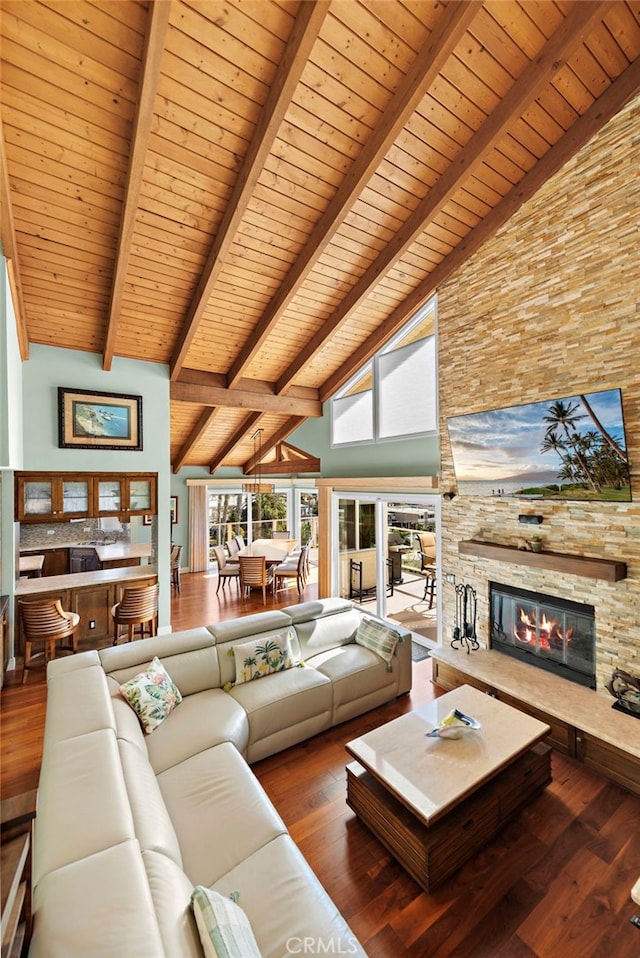 unfurnished living room featuring wood ceiling, hardwood / wood-style floors, high vaulted ceiling, a stone fireplace, and beamed ceiling