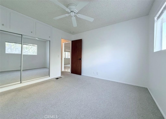 unfurnished bedroom featuring a textured ceiling, carpet flooring, visible vents, baseboards, and a closet