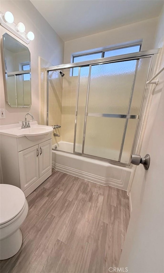 bathroom with toilet, enclosed tub / shower combo, wood finished floors, and vanity