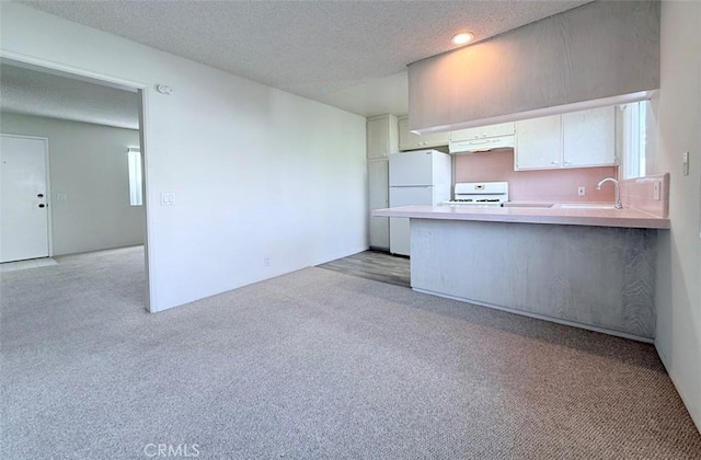 kitchen featuring under cabinet range hood, a peninsula, white cabinets, range, and freestanding refrigerator