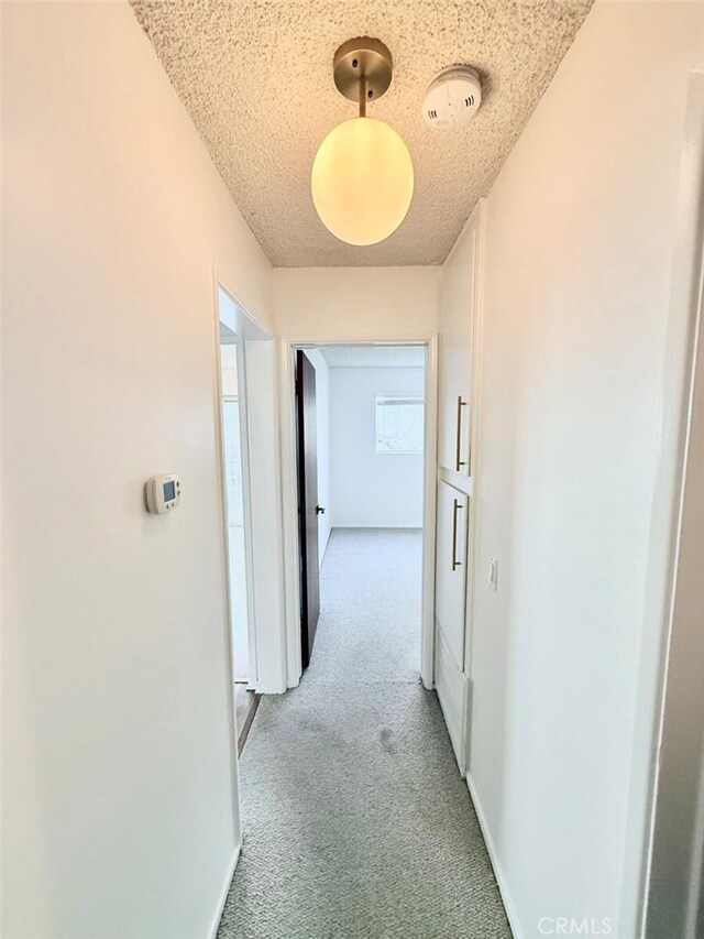 corridor with a textured ceiling and light colored carpet