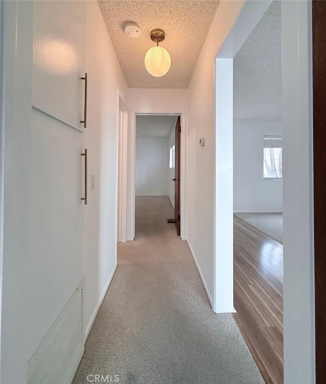 hallway with a textured ceiling, carpet floors, and baseboards