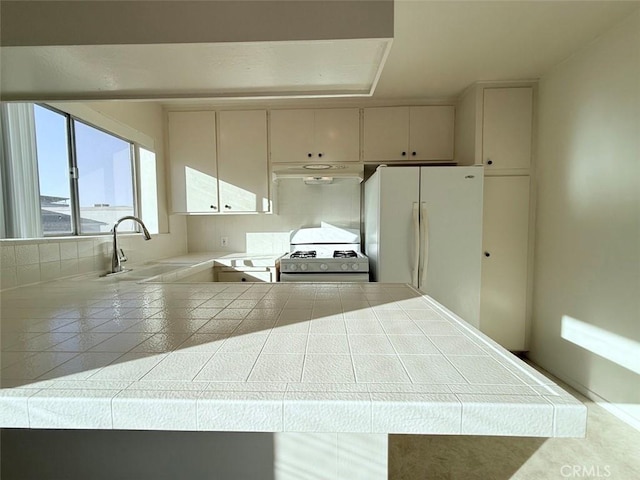 kitchen with under cabinet range hood, a peninsula, white appliances, a sink, and tile counters