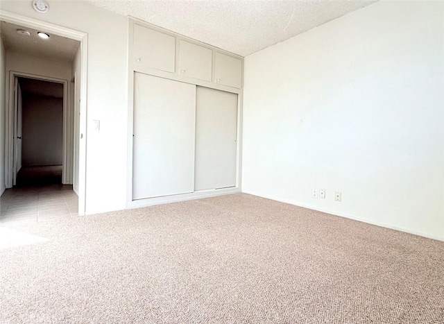 unfurnished bedroom featuring a textured ceiling, a closet, and light colored carpet