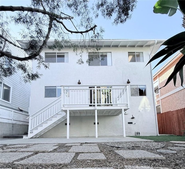 rear view of property with fence, stairway, and stucco siding