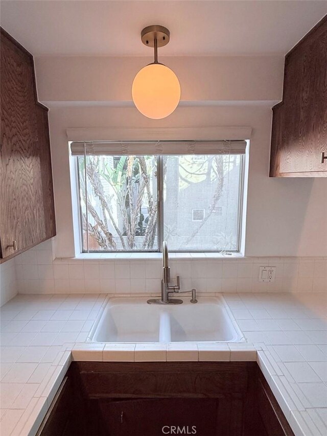 kitchen featuring tile countertops, dark brown cabinets, sink, and decorative light fixtures