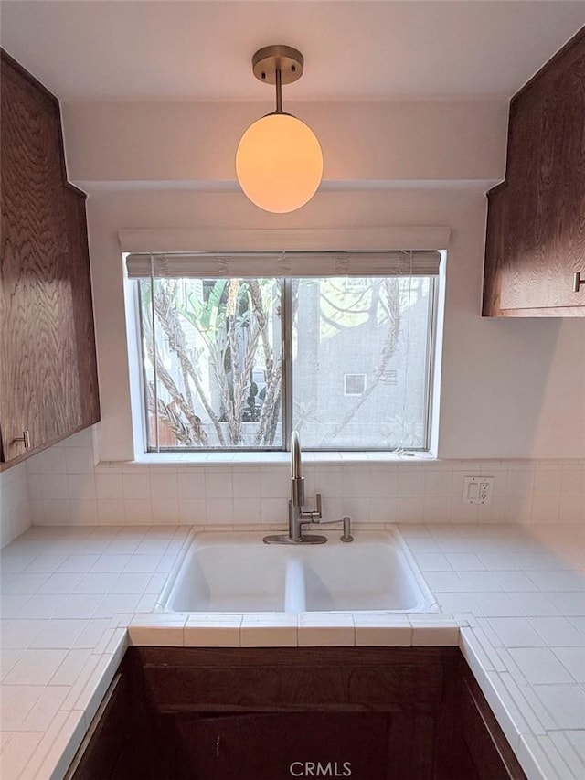 kitchen with tile countertops, dark brown cabinets, a sink, and a healthy amount of sunlight