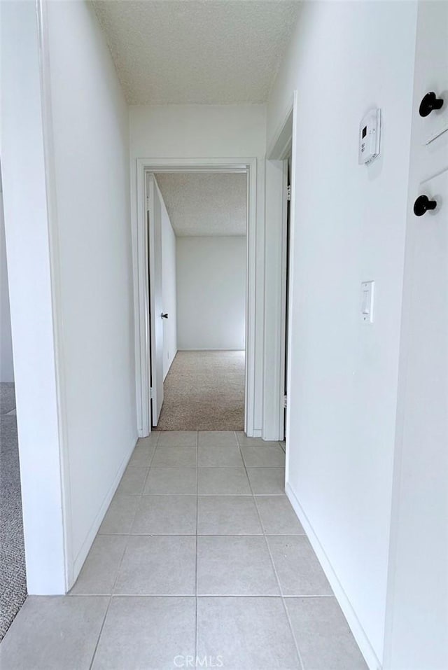 corridor featuring light tile patterned flooring, a textured ceiling, and baseboards