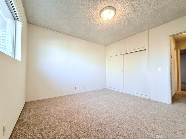 unfurnished bedroom with carpet, a textured ceiling, and a closet