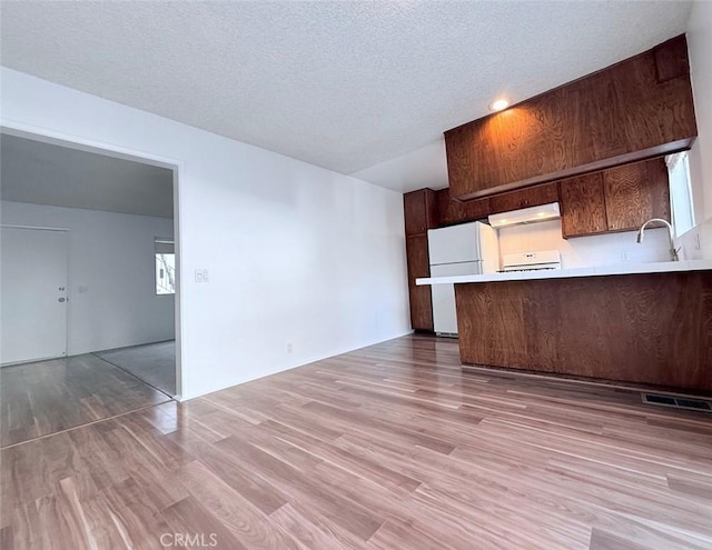 kitchen featuring light wood finished floors, light countertops, freestanding refrigerator, a peninsula, and under cabinet range hood