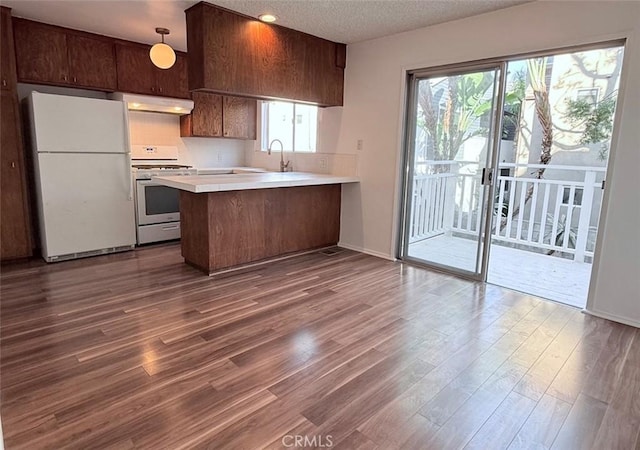 kitchen featuring dark wood-style floors, light countertops, a peninsula, white appliances, and under cabinet range hood