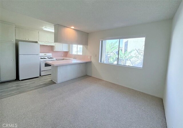 kitchen featuring kitchen peninsula, a textured ceiling, white appliances, light colored carpet, and range hood