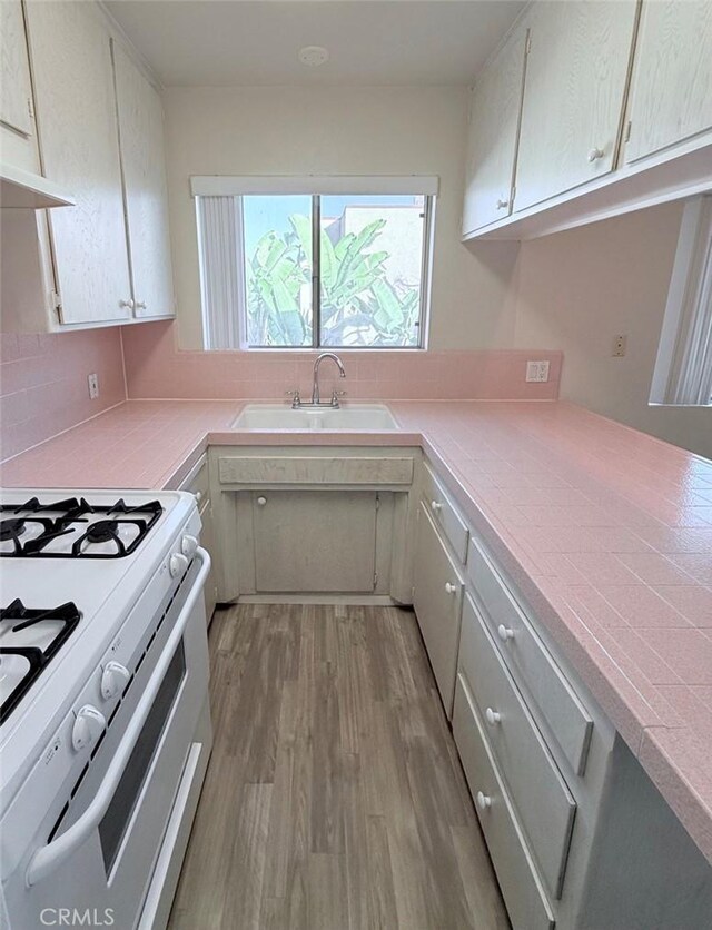 kitchen with sink, tile counters, light hardwood / wood-style flooring, white range with gas stovetop, and ventilation hood