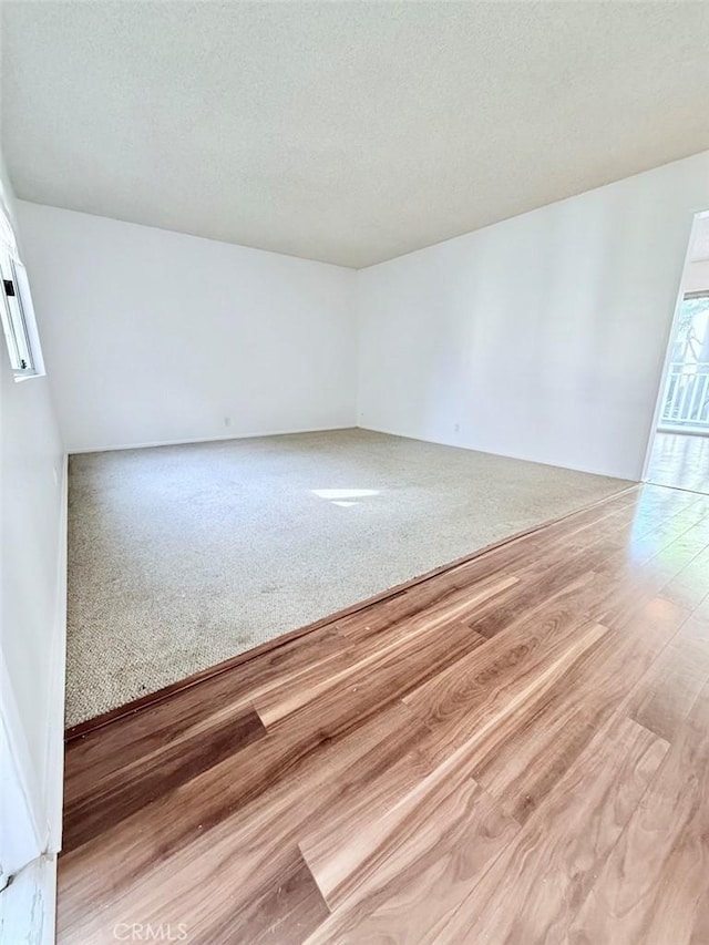 carpeted spare room with a textured ceiling and wood finished floors