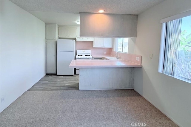 kitchen with a textured ceiling, a peninsula, white appliances, a sink, and light countertops