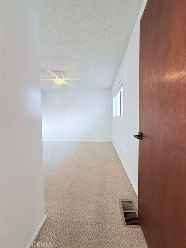 carpeted spare room featuring a ceiling fan, visible vents, and a textured ceiling