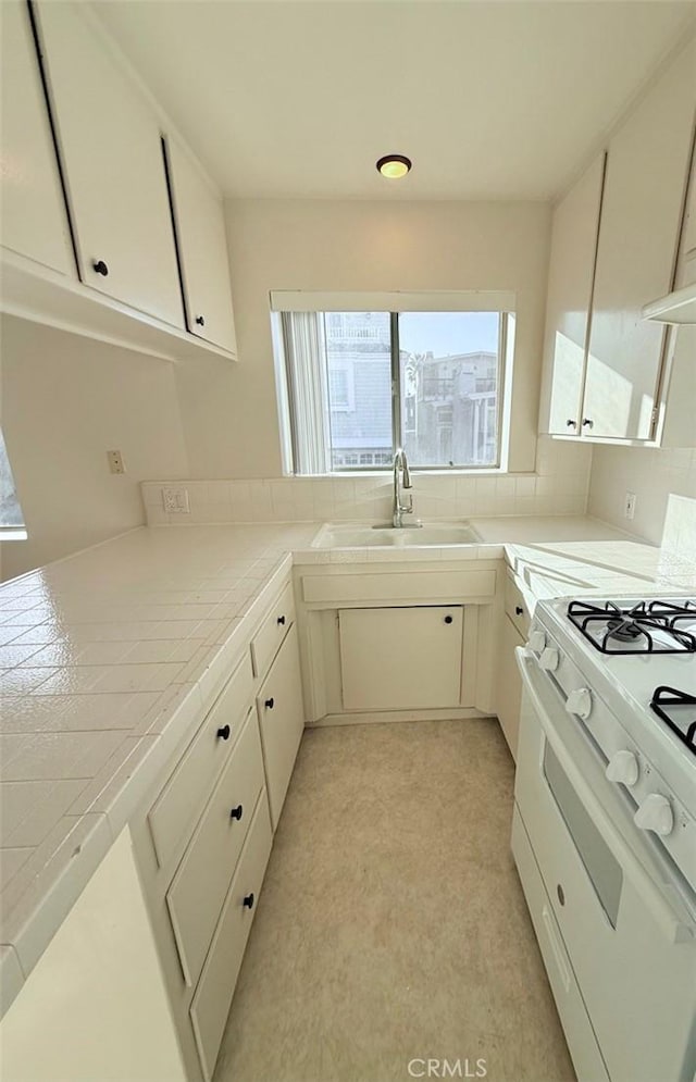 kitchen with white cabinetry, white gas range oven, tile counters, and a sink