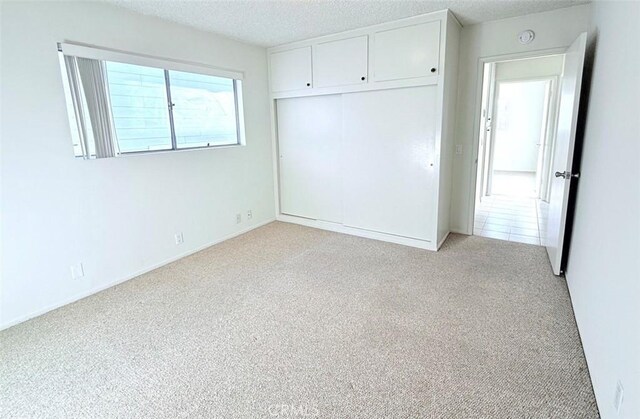 unfurnished bedroom featuring light carpet, a textured ceiling, and a closet