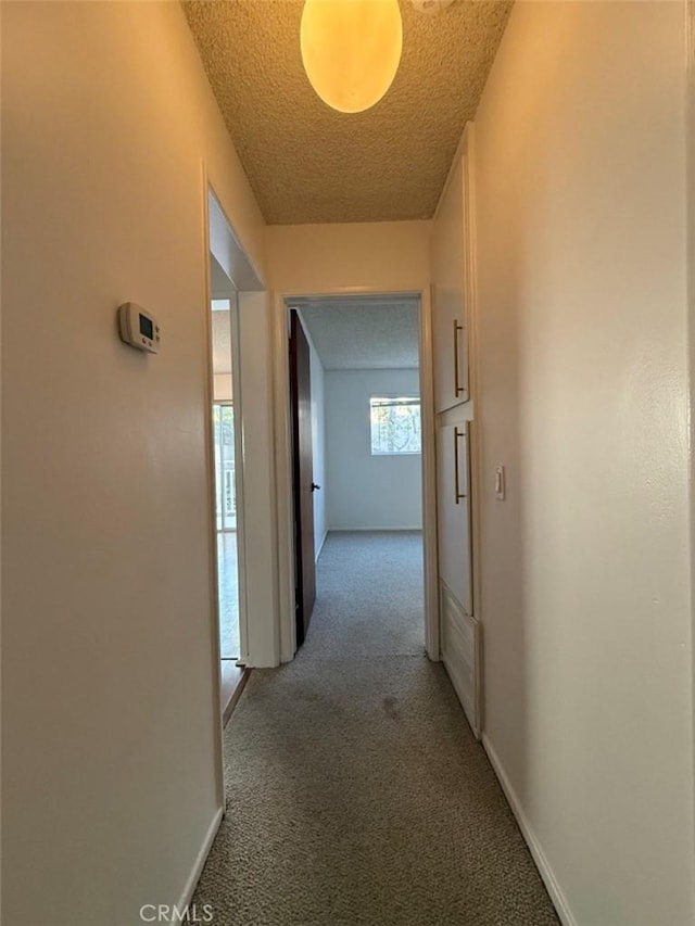 hallway featuring light carpet, a textured ceiling, and baseboards