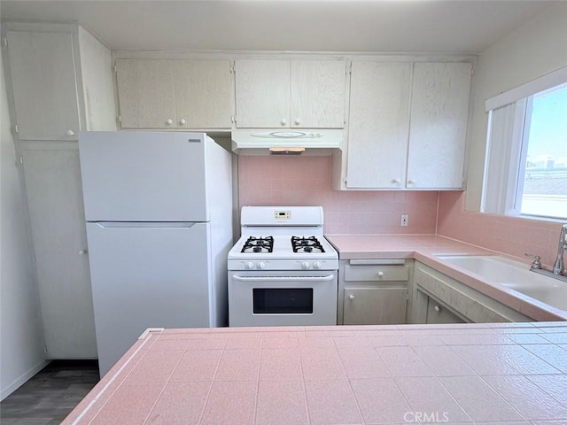 kitchen with white appliances, tasteful backsplash, wood finished floors, under cabinet range hood, and a sink