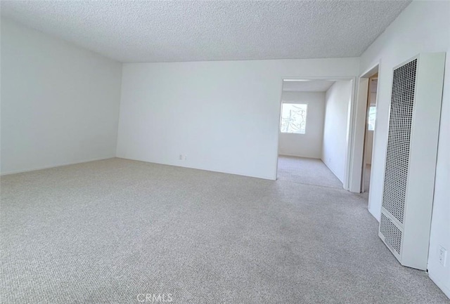 empty room featuring a textured ceiling, a heating unit, and light colored carpet