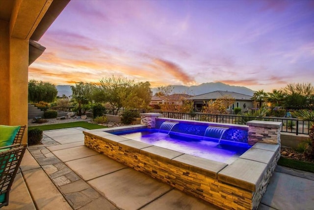 pool at dusk with an outdoor hot tub, a patio area, and pool water feature