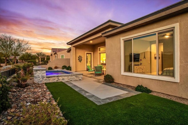 back house at dusk with a lawn and a patio area