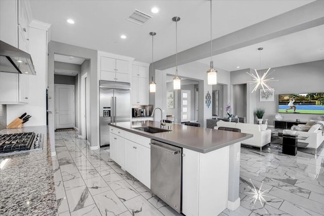 kitchen with sink, appliances with stainless steel finishes, pendant lighting, a kitchen island with sink, and white cabinets